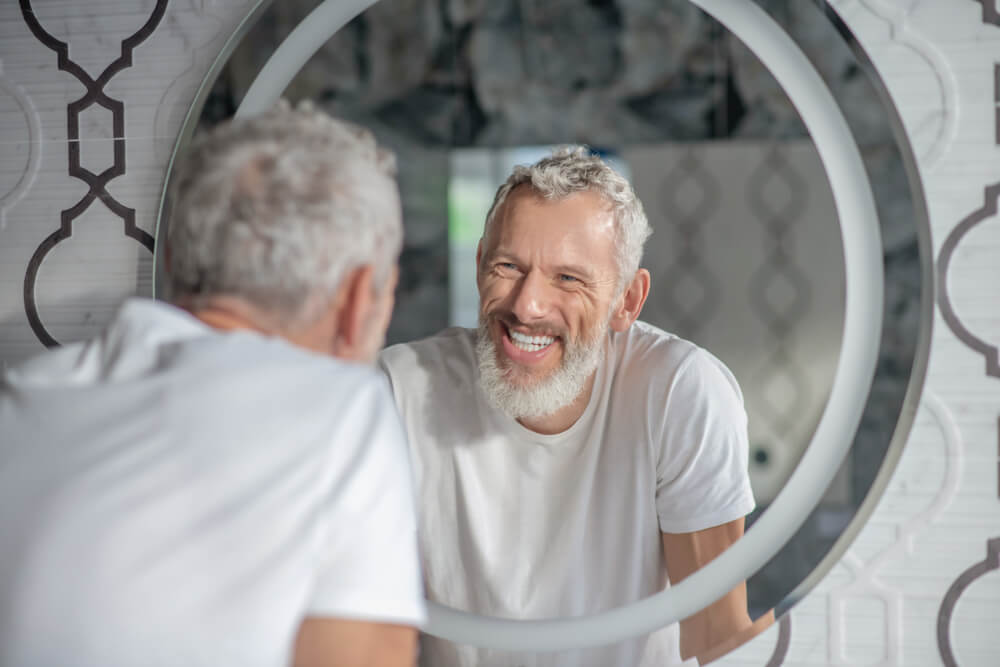 smiling grey-haired man looking at the mirror