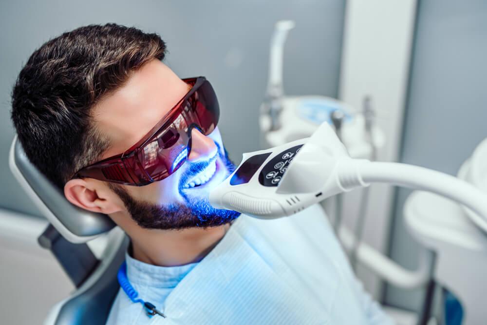 Dentist doing teeth whitening procedure with young man